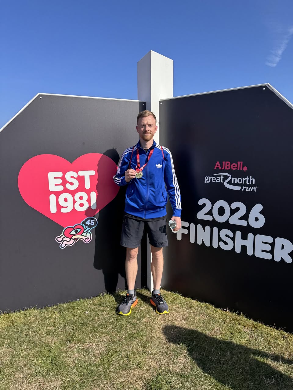 Elliot wearing his medal in front of the Great North Run 2026 finisher poster